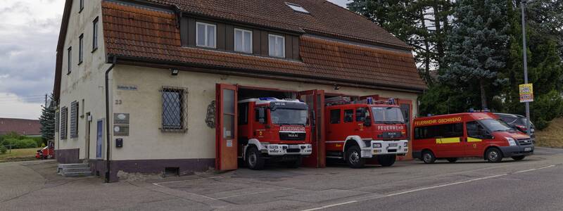Ein Feuerwehrhaus mit zwei geparkten Feuerwehrautos und einem Feuerwehreinsatzfahrzeug davor.