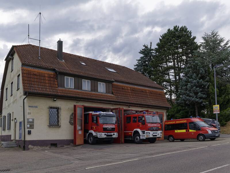 Ein Feuerwehrhaus mit zwei geparkten Feuerwehrautos und einem Feuerwehreinsatzfahrzeug davor.
