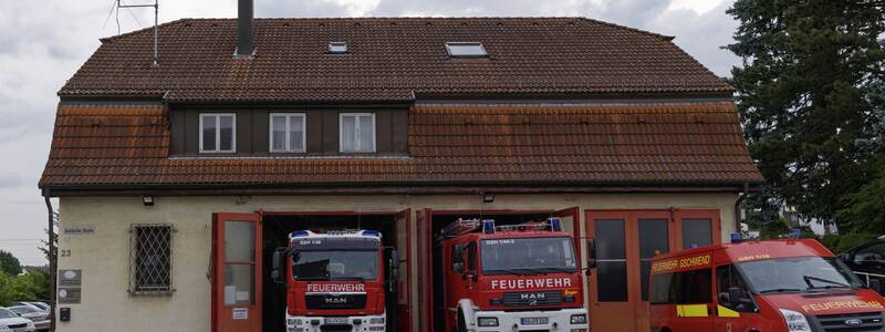 Vor einem Feuerwehrgebäude mit schrägem Ziegeldach stehen zwei rote Feuerwehrfahrzeuge eines deutschen Feuerwehrkorps.