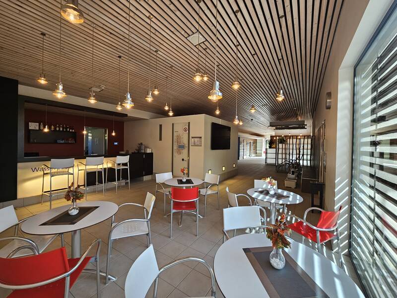 Ein moderner, gemütlicher Cafébereich mit runden Tischen und bunten Stühlen, beleuchtet von stilvollen Hängelampen.