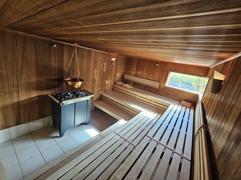 Eine holzverkleidete Sauna mit mehreren Sitzbänken, einem Ofen und einem Fenster, das Tageslicht hereinlässt.