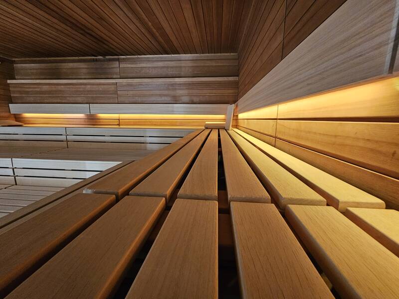Holzvertäfelte Sauna mit beleuchteten Sitzbänken und Wänden aus warmem Holz.
