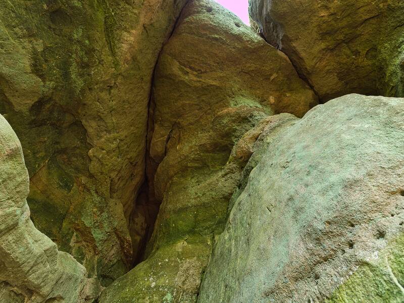 Große, raue Felsen bilden eine schmale Felsspalte, die nach oben geöffnet ist, mit überwiegend grünlichen und bräunlichen Tönen.