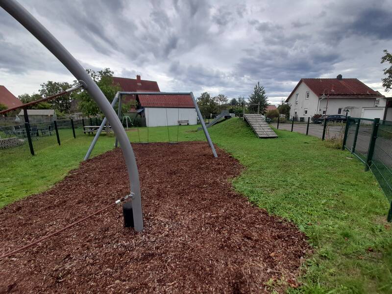 Ein Spielplatz mit einer Seilbahn und Grünflächen, umgeben von Wohnhäusern und einem trüben Himmel.